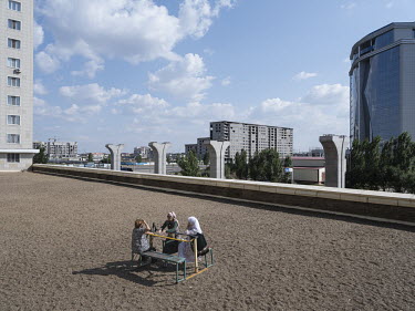 Three women sit on a rooftop. In the background the KEGOC-building and the pillars of the incomplete Light Rail Transit (LRT) can be seen. The LRT is allegedly unfinished due to corruption.