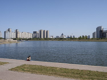A couple sit on the banks of the Ishim river. The pyramid in the background is the Palace of Peace and Reconciliation, a conference center, designed by Norman Foster.