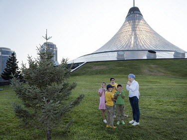 A faimly stands next to a pine tree in front of the Khan Shatyr shopping and entertainment center, designed by Norman Foster. It is the highest tensile structure in the world. It houses a shopping mal...