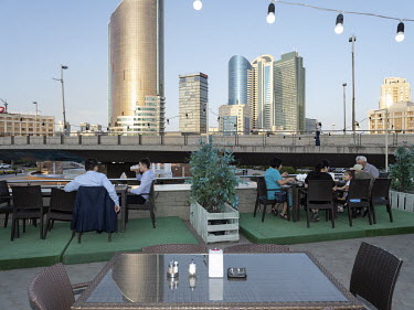 Diners sit at tables outdoors at a restaurant with a view of high rise buildings on Nurzhol Boulevard.