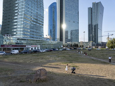 People walk across a patch of grass in front of highrise buildings along Nurzhol Boulevard.