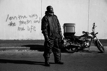 Mande, a Congolese migrant in South Africa, takes pride in his work as a food delivery rider. Here he poses next to his bike and a graffito on the wall which reads 'I am the way, the truth and the lif...