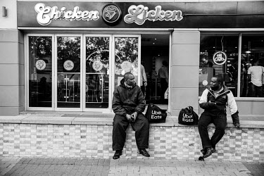 Congolese migrant Mande (left), a food delivery rider, sits next to another rider while they wait to take a food delivery at Chicken Licken restaurant.