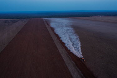 A tractor spreads lime to prepare soil on a large field on a mechanised farm next to Irantxe Manoki indigenous land in the background.