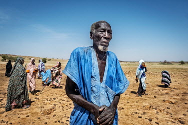 An older man coordinates female workers. The women remove stones to improve the land for agriculture. The stones will be used to build a dam to irrigate the land when it rains.