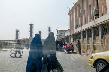 Two women wearing burqas cross a street in the city centre.