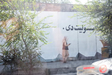 People walk past the protective concrete walls of administrative buildings which were covered with peace murals but have been repainted with phrases in praise of Islam and the Islamic Emirate of Afgha...