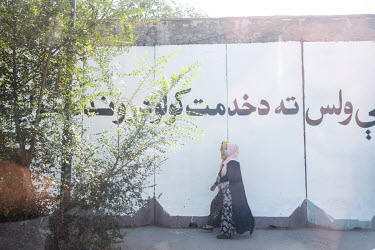 People walk past the protective concrete walls of administrative buildings which were covered with peace murals but have been repainted with phrases in praise of Islam and the Islamic Emirate of Afgha...