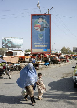 A woman wearing a burqa crosses a road in front of an advertisement for a school which includes the slogan 'Seeking the Light' and features a photo of a young female student. The billboard is topped w...