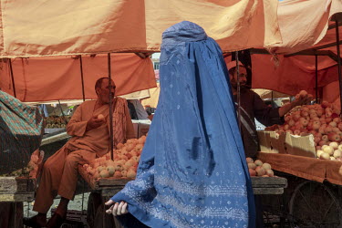 A woman wearing a burqa walks past stalls welling apples in a busy street market.