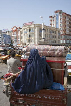 A woman in a burqa travels in the back of a vehicle through a street market.