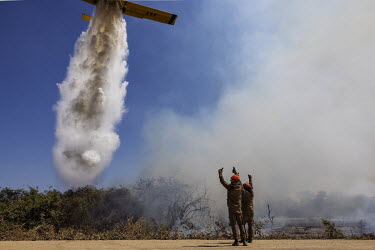 Firefighter give a thumbs up as a plane drops water over a fire on the banks of the Transpantaneira road, in Mato Grosso.