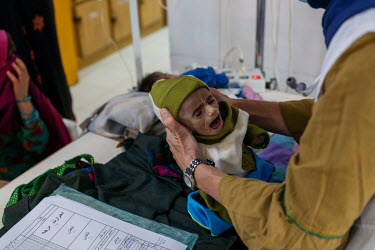 A Medecins Sans Frontieres (MSF) staff member holds a severely malnourished child in a therapeutic feeding unit at MSF Lashkar Gah hospital, where each bed is occupied by two children.