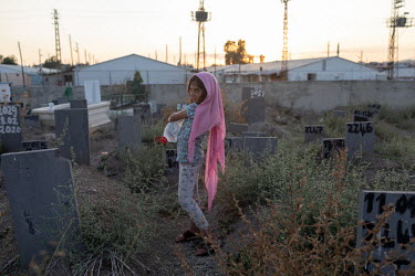 A young girl selling water to people visiting a cemetery where tens of migrant's, whose identities are unknown, and instead are listed by numbers.