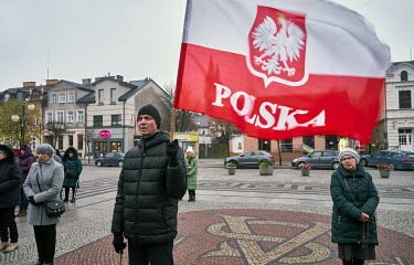 An elderly man with a patriotic polish flag prays during a mass organised by the brothers of the Rosary community, on the square in Augustov. In the autumn weather, the brothers offered dozens of peop...