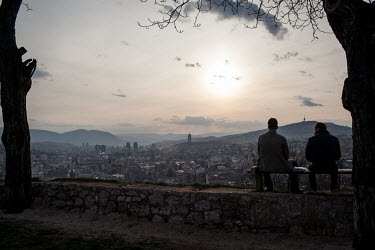 Locals sit on a hill top overlooking Sarajevo at sunset.