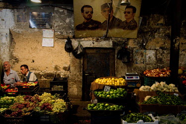 Posters of Syria's former president Hafez al-Assad (top centre), with his son current president Bashar al-Assad (top right) and other son Bassel Al-Assad (top left) hang above a fruit and vegetable ma...