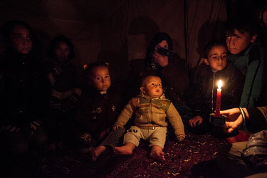 Ebtisam Hammud (centre) holds her young son Ahmed, in their tent lit only by candle light and without electricity or heating in Atmeh camp where more than 12,000 diplaced Syrians are living.