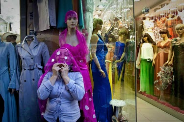 A women's clothing store salesperson hides her face under the dress of a model, along the enterance to the Grand Bazaar.