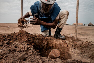 A Mines Advisory Service (MAG) de-miner digs out a suspected unexploded ordnance next to a busy market which was uncovered by a grader repairing a road.