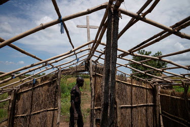Charles Okalonam walks past the new church he is building on land that was once a minefield. 22 people have returned so far and all come to this church. "This is our ancestral land, it is good land. W...
