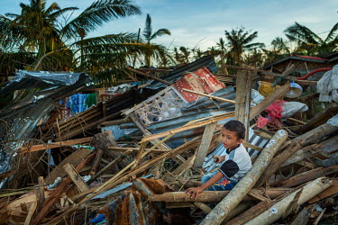 'Impoy' Prince Jhay Mark Timonio (8) sits in the debris of destroyed houses in Barangay Tapon in the aftermath of typhoon Rai.  The impact in this area was immense. Almost all of the houses in this di...