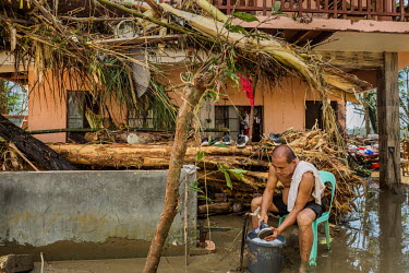 Marcelo Tumanda (56) sits in front of his house in the barangay of Valladolid and washes a pair of shoes. Tumanda, his family and neighbours took refuge on the second floor of the house but with an es...