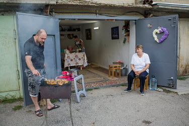 A man cooks chicken on a barbeque as a family prepares for a reunion gathering at their garage.