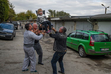 A little girl celebrating her birthday at a garage used as an extra space is lifted up and down on a chair by family and friends. A local tradition is that the person being celebrated is lifted into t...