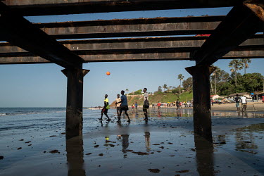Youths play football on the beach, beside a metal jettty.