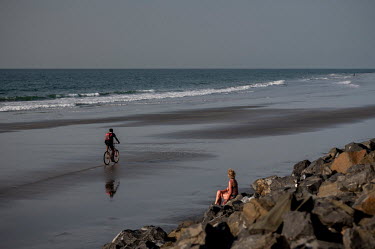 A cyclist risea along a beach where a lone tourist sunbathes on a water break. Hotels along Senegambia's beaches are trying to protect themselves from the rising waters due to climate change by buildi...