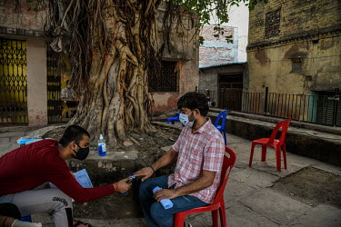 A volunteer uses an oximeter to check the blood oxygen saturationof a patient with COVID-19 symptoms before they have a consultation with a volunteer doctor at a community centre, under a Banyan tree...