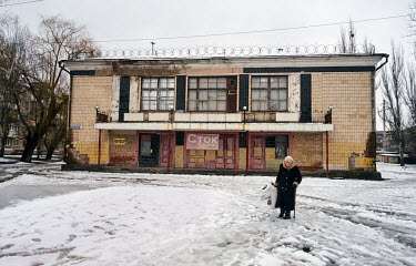 Lyuba, 68, walks past the former cinema. She remembers going to watch most of the movies that were shown there. Luyba carries a bag full of cartons, which she collects for reuse. She gets 3 hryvnia (0...