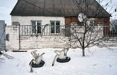 Swans cut from tires stand in front of a house in the snow.