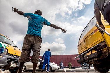 A bus conductor stands at one of the bus stops in Oshodi, a busy transportation hub on Lagos Mainland, touting for passengers for commercial buses ('Danfo') parked on the roadside.