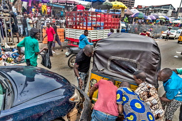 A group of men lift a tricycle rickshaw that has become tangled with the bumper of a car after a collision on Nnamdi Azikiwe street on Lagos Island.