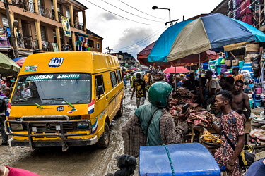 A yellow commercial bus passes stalls in Oshodi market.