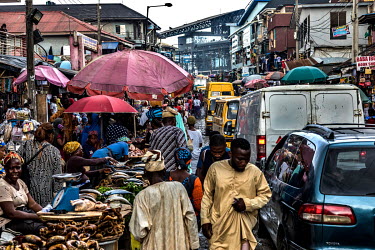 Yellow commercial buses and other vehicles pass stalls selling fish and meat in Oshodi market.