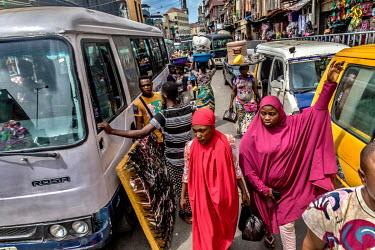 Pedestrians navigating the narrow spaces between passenger vehicles at the Idumota Market on Lagos Island.