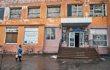 A woman passes a bakery where the windows on the second floor are covered by metal sheets rep[lacing the glass that shattered when artillery fire hit nearby.