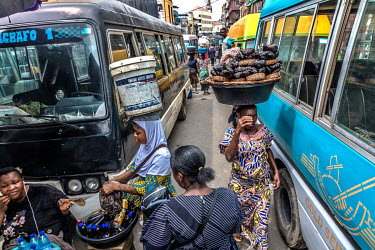 Vendors of cold drinks and smoked catfish navigating the narrow spaces between passenger vehicles at the Idumota Market on Lagos Island.