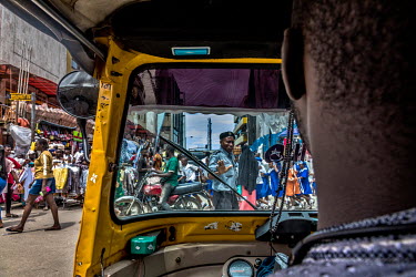 A tricycle rickshaw navigating the narrow spaces between passenger vehicles at the Idumota Market on Lagos Island.