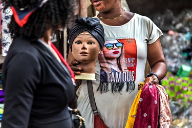 A street vendor selling headscarfs holds a mannequin display head in Oshodi market.