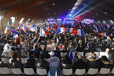 Supporters of far right presidential candidate Eric Zemmour wave French national flags at a rally in Burgundy while Zemmour is speaking.