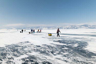Tourists are travelling by foot along the Ice of Baikal lake. During the winter period, the ice surface of Baikal becomes a main transport route between different settlements and the island.