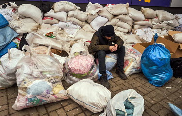 A young man rests on plastic bags filled with donated blankets. Residents of Dnipro have been bringing clothes, mats, canned food, cigarettes, bottled water and more. Volunteers then sort all donated...