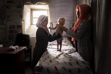 Hojatullah (11 months old) with his mother Afisa (25) (left) are seen by a health worker in a small clinic managed by UNICEF. Children from the village of Alibeg and surrounding area are being medical...