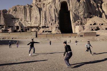 Young people playing football in front of the site of the Buddhas of Bamiyan, cliffs where the huge Buddha statues stood until being destroyed by the Taliban in 2001.