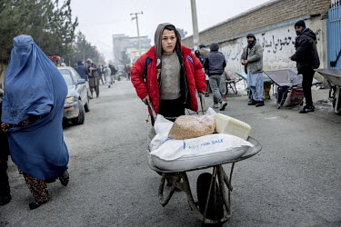 A boy earns some money by acting as a porter, using a wheelbarrow to move sacks of food distributed by the World Food Program (WFP) to starving Afghan families. People had been waiting all morning to...