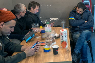 Delivery drivers and kitchen volunteers look at their phones during a wait for a batch of meals to be delivered to the front line at the Food vs Marketing army meals project.